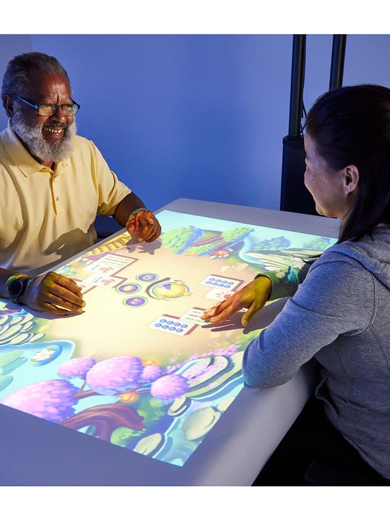 Older adult playing a projected tabletop game with a caregiver on Southpaw Obie Pro